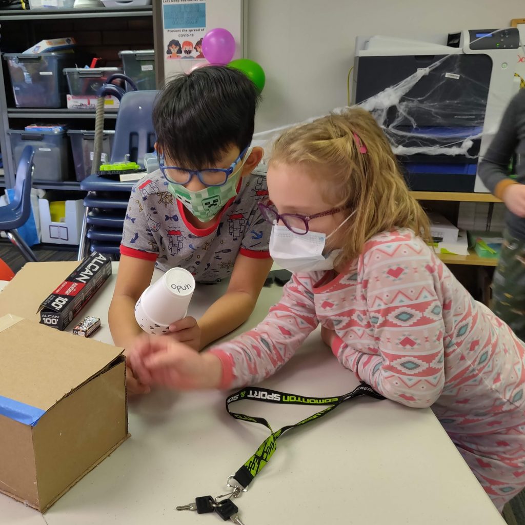 Children in Masks create crafts with cardboard box at Discover Coding.