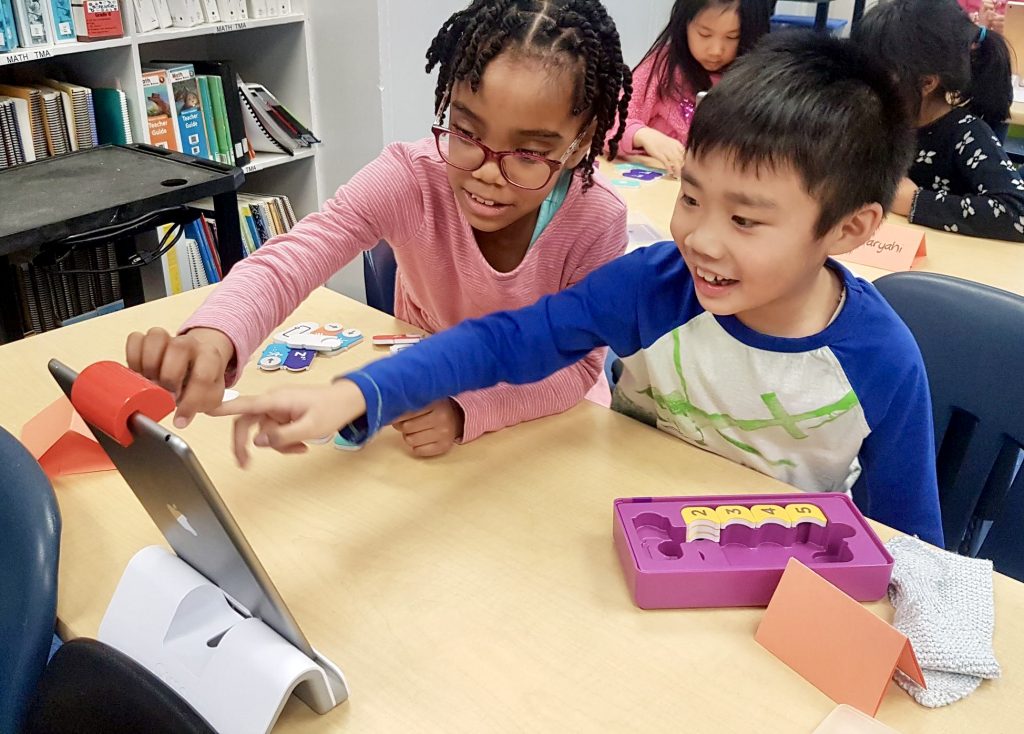 Image of two children learning Scratch coding and pointing at an iPad together.