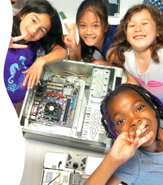 Group of young women smile at the camera while posing next to an open computer.